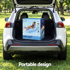 A boxed inflatable pool float lounger sits in the open trunk of a white SUV parked on grass in a park. The box shows a blue and white design with an illustration of a person floating on the product.
