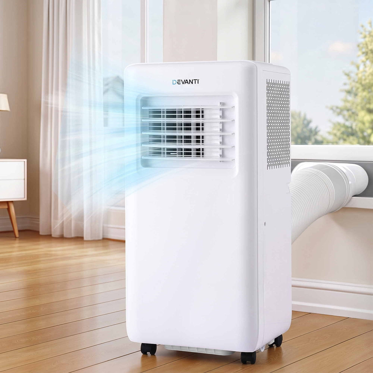 A white Devanti portable air conditioner with a flexible white duct connected to a window, shown in a bright room with wooden floors and white curtains. Blue light rays are illustrated coming out of the front vent.