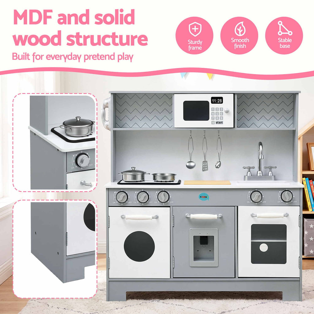 A children's MDF play kitchen set shown in a staged room scene with promotional text and feature icons. The kitchen has a gray wood-grain frame, white cabinets and countertops, toy stovetops with pots and pans, hanging utensils, a sink, and toy appliances.