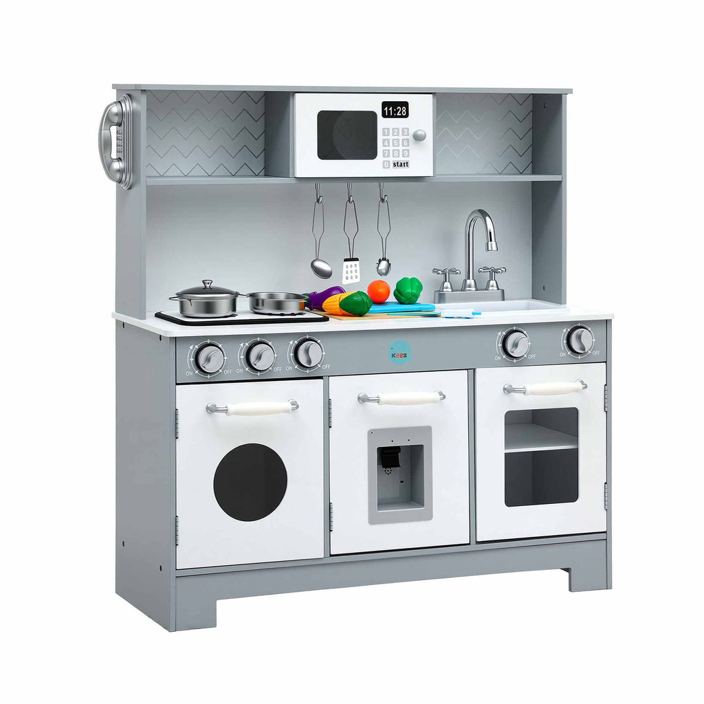 A children's toy kitchen playset with a gray and white faux-wood design, featuring three oven doors, a stovetop with pots and pans, a sink with a faucet, hanging utensils, a shelf with a toy microwave, and colorful toy fruits and vegetables on the counter.