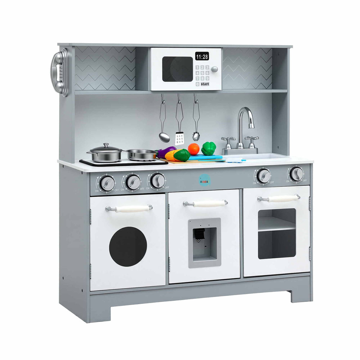 A children's toy kitchen playset with a gray and white faux-wood design, featuring three oven doors, a stovetop with pots and pans, a sink with a faucet, hanging utensils, a shelf with a toy microwave, and colorful toy fruits and vegetables on the counter.