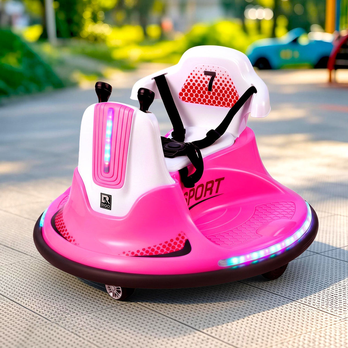 A pink and white electric bumper car ride-on toy with LED lights, shown outdoors on a paved path with a blurred background.