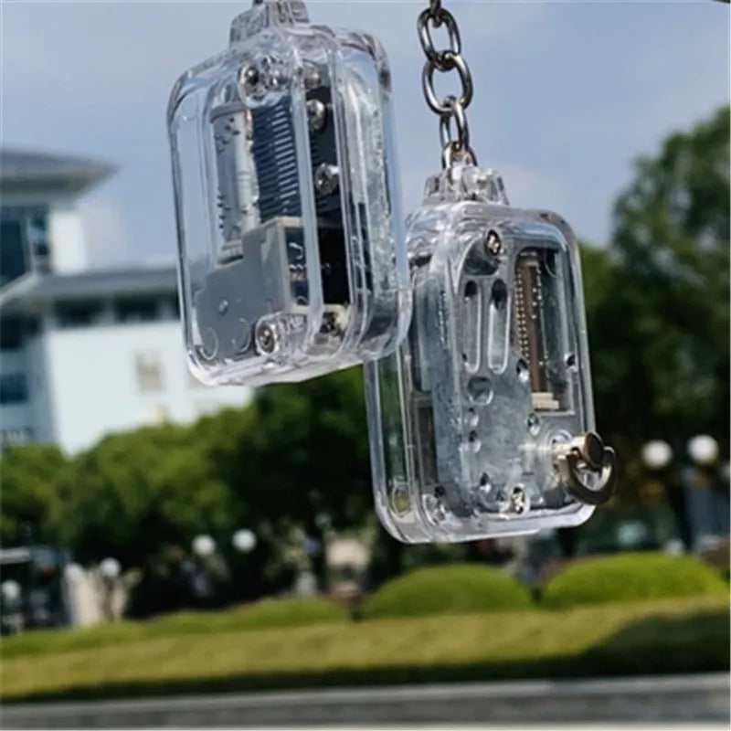 Two transparent mechanical keychains hanging against a blurred outdoor background.