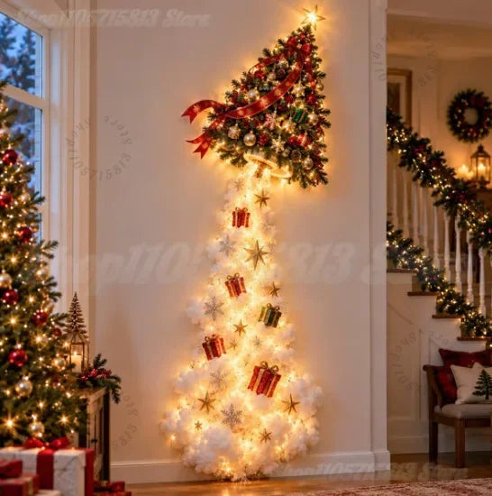A tall, narrow Christmas tree decoration with a star-topped green top, warm white string lights, red ribbon, and small gift and snowflake ornaments, displayed indoors against a cream wall in a decorated holiday home.
