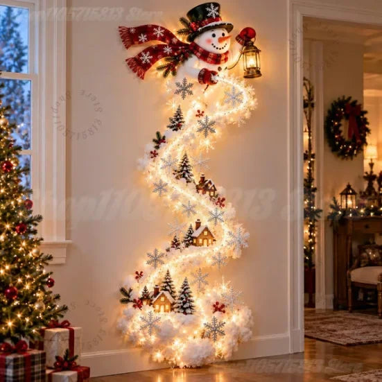 A festive Christmas wall decoration shaped like a spiral staircase, featuring a smiling snowman at the top, warm white string lights, white snowflakes, small evergreen trees, cozy house motifs, and red berry accents, displayed in a decorated home interior next to a Christmas tree.