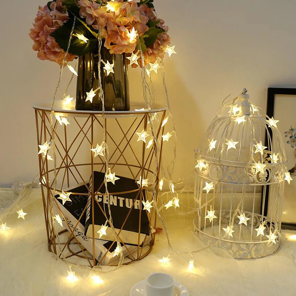 Decorative setup with star lights, a vase with flowers, and a birdcage on a table.