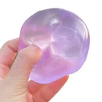 A hand holding a translucent purple and lavender gel-like stress toy against a plain white background.