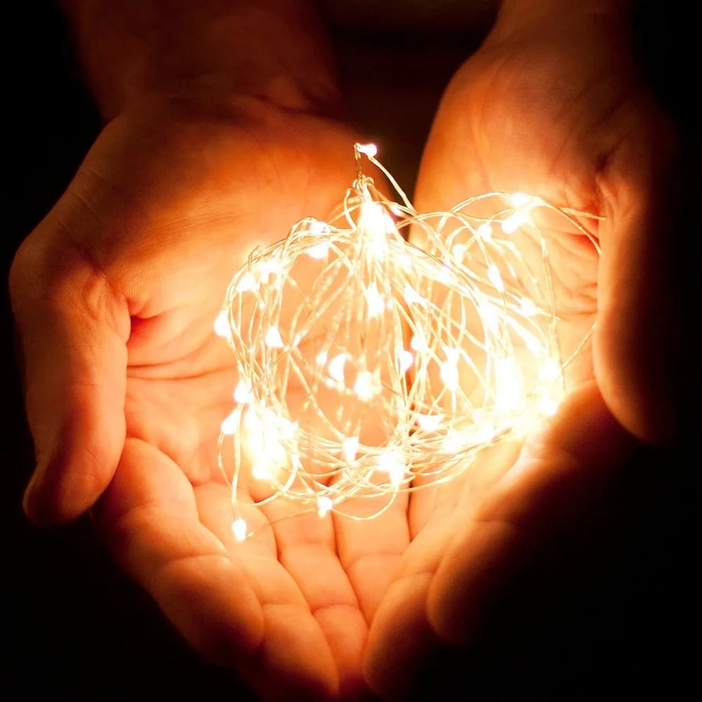Hands holding a string of small lights against a dark background