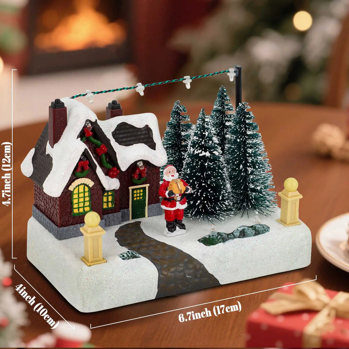 Decorative Christmas scene with a house, trees, and Santa Claus on a wooden table.
