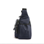 A navy blue nylon sling backpack with multiple zippered compartments and black trim, shown from a side profile view on a white background.
