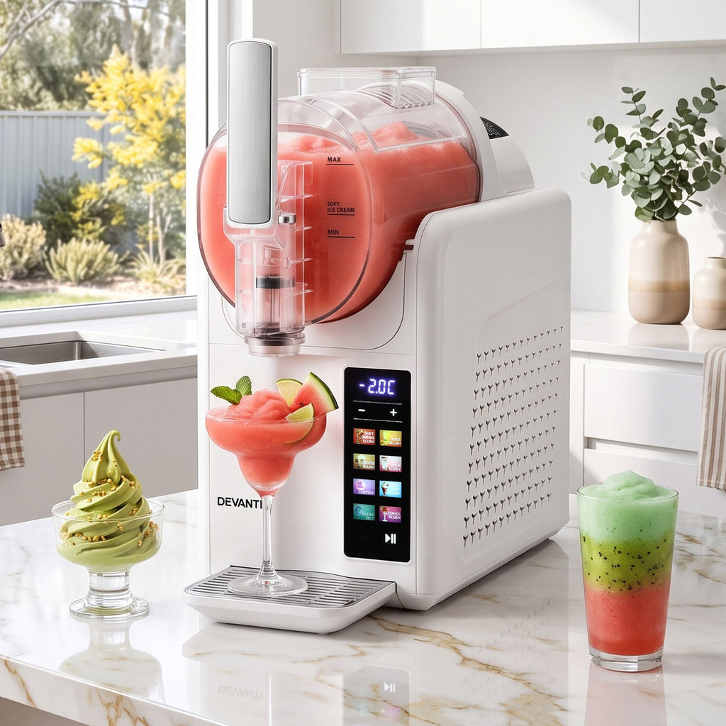 A Devanti slushie maker machine on a marble kitchen counter, shown dispensing a pink slushie into a glass with lime and mint garnish. The machine has a white body, a clear hopper filled with pink slushie, and a digital control screen on the front.