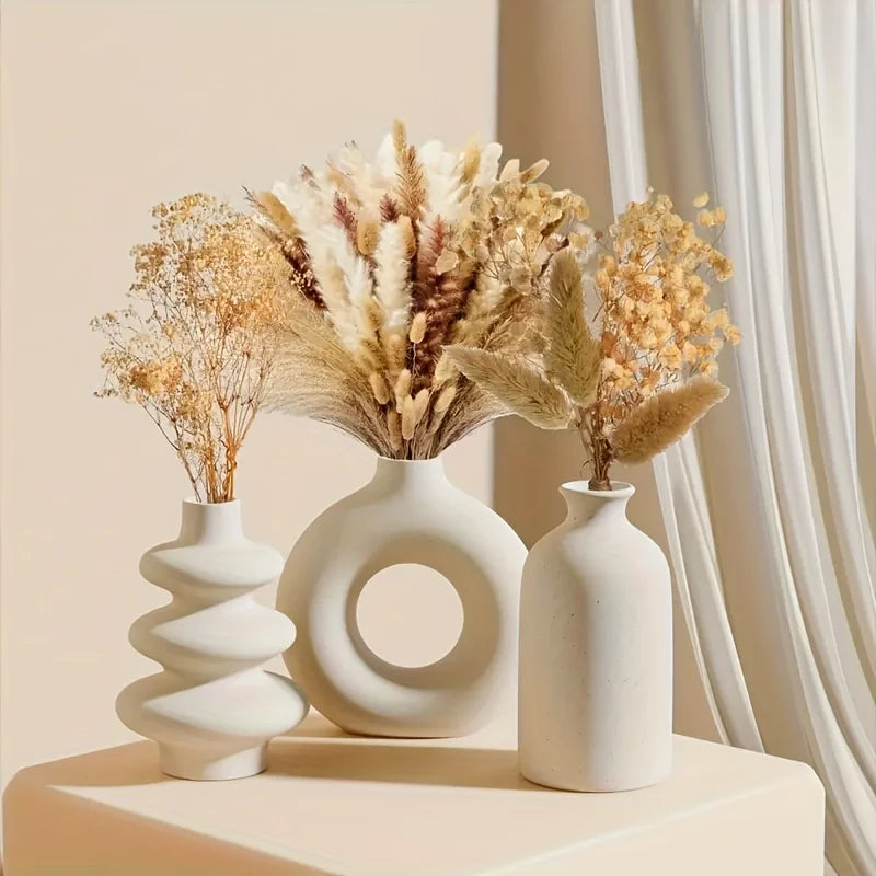 Three white vases with dried floral arrangements on a beige surface.