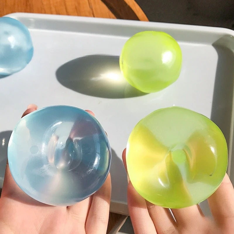 Two hands holding a blue and green translucent ball against a white tray.