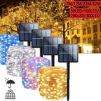 Solar string lights shown with four black solar panels and four wire rolls in blue, clear/white, purple, and warm white/gold. The background is a nighttime city street with lit trees and buildings, plus text indicating light counts from 7W to 300LED.