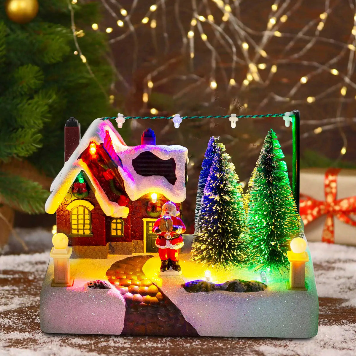 Decorative Christmas scene with a house, trees, and Santa Claus figure, illuminated by colorful lights.