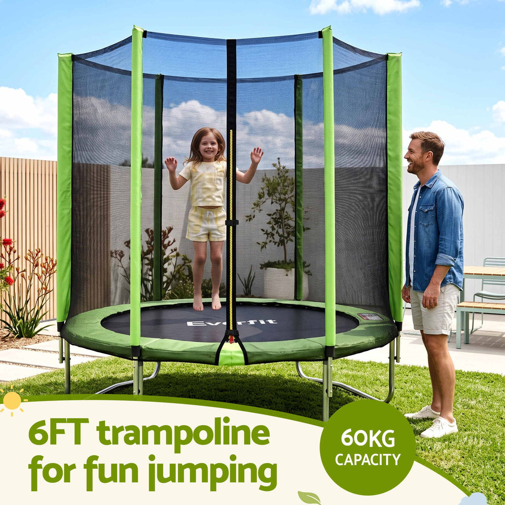 A round outdoor trampoline with a green safety net enclosure is shown in a backyard setting. A child is jumping on the trampoline while a man stands beside it.