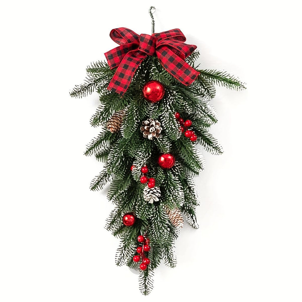 A hanging Christmas wreath decoration made of green pine branches with white frost, a red and black buffalo plaid bow at the top, red ornaments, pinecones, and red berry clusters, shown on a plain white background.