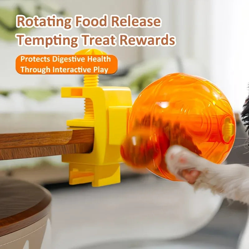 A pet treat dispenser toy with a yellow clamp and an orange translucent ball being pushed by a cat's paw, with promotional text overlaid at the top.