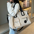 Person holding a large beige bag with black accents in an indoor setting.