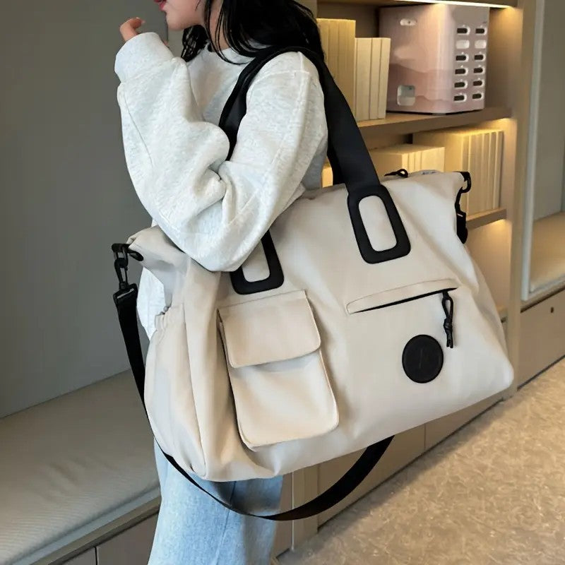 Person holding a large beige bag with black accents in an indoor setting.