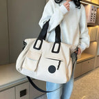 Person holding a white tote bag with black accents in an indoor setting