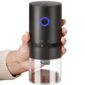 Hand holding a black pepper grinder with a clear body and blue light on a white background
