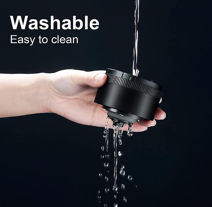 Black shower head held by a hand with water flowing, against a black background.