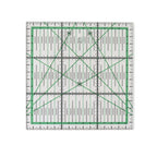 A square clear acrylic quilting ruler with green grid lines, black measurement markings, and diagonal crosshairs on a white background.