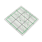 A clear acrylic quilting ruler with green and black measurement markings, shown at an angle on a plain white background.