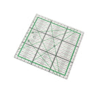 A clear square quilting ruler with green grid lines and black measurement markings, shown at an angle on a plain white background.