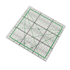 A square quilting ruler with a clear plastic body, featuring green grid lines, black measurement markings, and a green border, shown on a plain white background.
