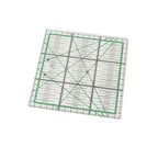 A clear acrylic quilting ruler with green grid lines and black measurement markings, shown at an angle on a plain white background.