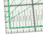 A close-up of a clear acrylic or plastic ruler with green measurement markings and black grid lines on a white background.