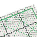 A close-up of a clear acrylic quilting ruler with green and black measurement markings, showing a 90-degree corner and a central hole.