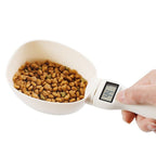 Digital pet food measuring cup with a bowl of kibble on a white background