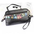 Black pebbled leather crossbody handbag with a colorful floral pattern panel across the front, gold-tone hardware, a wristlet strap, and a shoulder strap, shown on a white background.