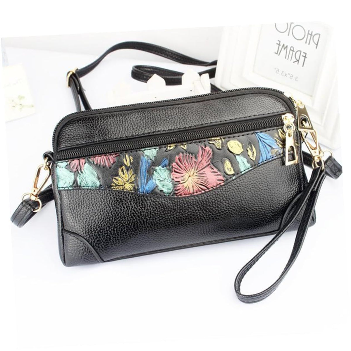 Black pebbled leather crossbody handbag with a colorful floral pattern panel across the front, gold-tone hardware, a wristlet strap, and a shoulder strap, shown on a white background.
