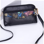 Black pebbled leather crossbody bag with a colorful floral patterned front pocket, gold-tone hardware, and a detachable shoulder strap on a white background.