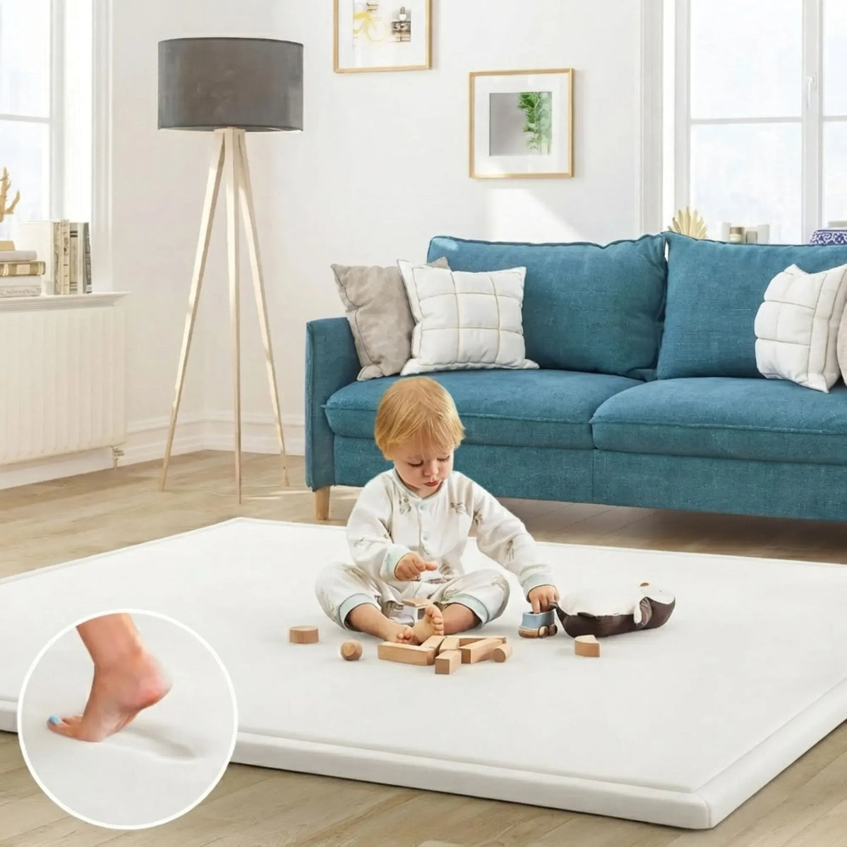 A child sits on a thick white mattress on the floor in a bright living room with a blue sofa, lamp, and framed wall art. A circular inset shows a close-up of a foot pressing into the mattress surfac