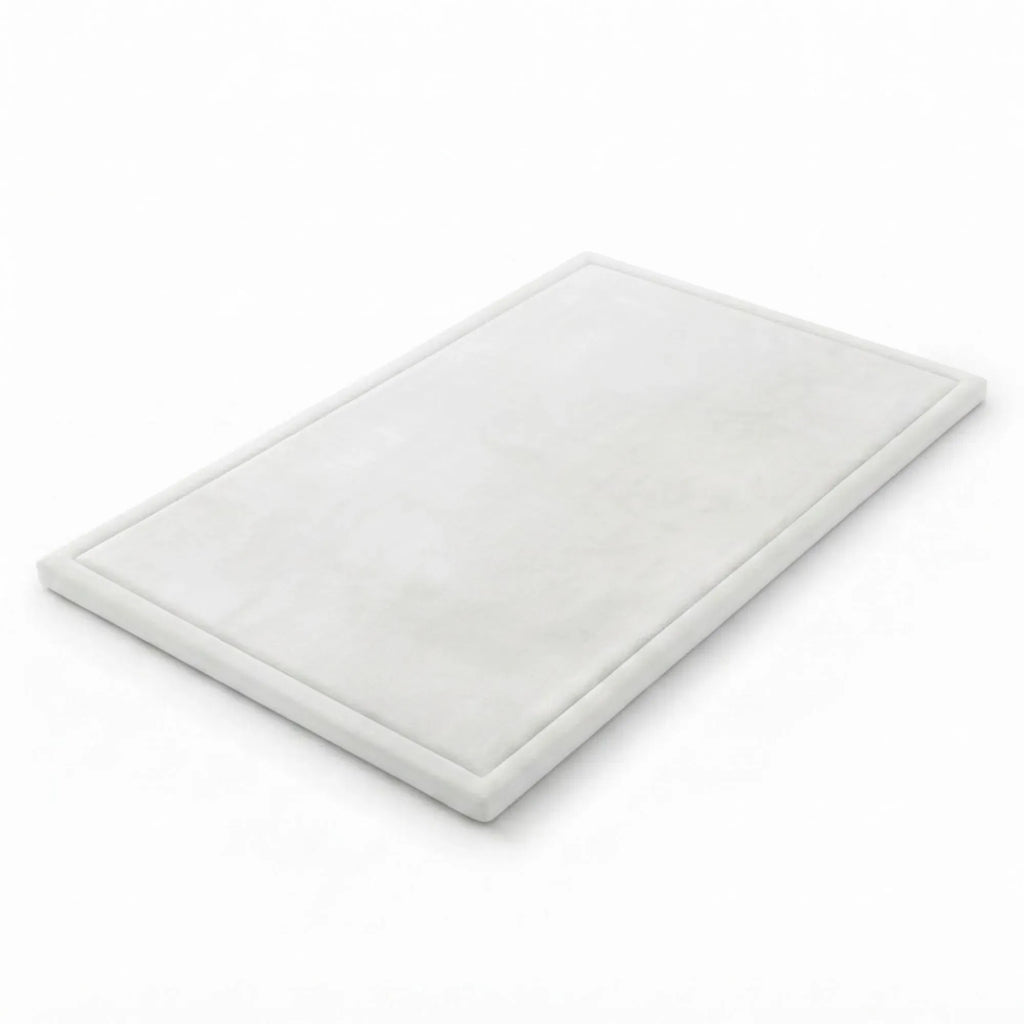 A rectangular white marble cutting board with a raised border, shown at an angle on a seamless white background.