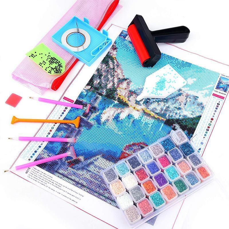 Diamond painting kit with a printed mountain landscape canvas, multicolor beads in a clear plastic tray, paint sticks, a mesh bag, a squeegee, and a roller tool on a white background.