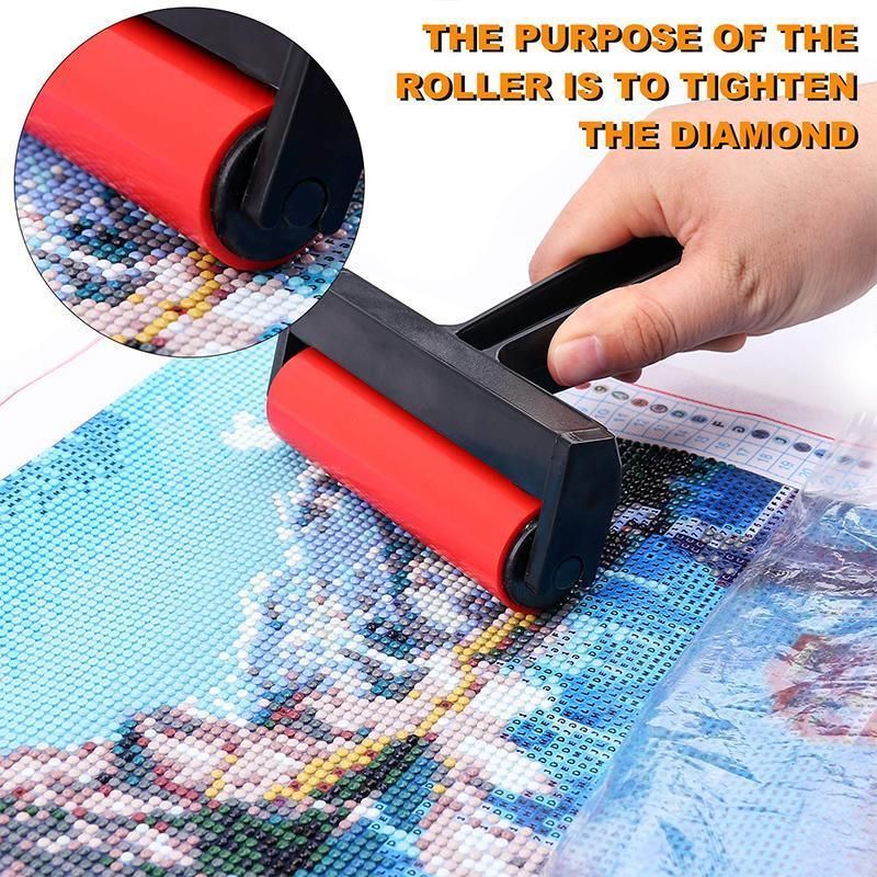 A hand holds a red and black diamond painting roller over a colorful canvas, with an inset circle showing a close-up of the roller and orange text reading 'THE PURPOSE OF THE ROLLER IS TO TIGHTEN THE DIAMOND'.
