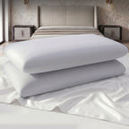 wo white pillows stacked on a bed in a bedroom setting.