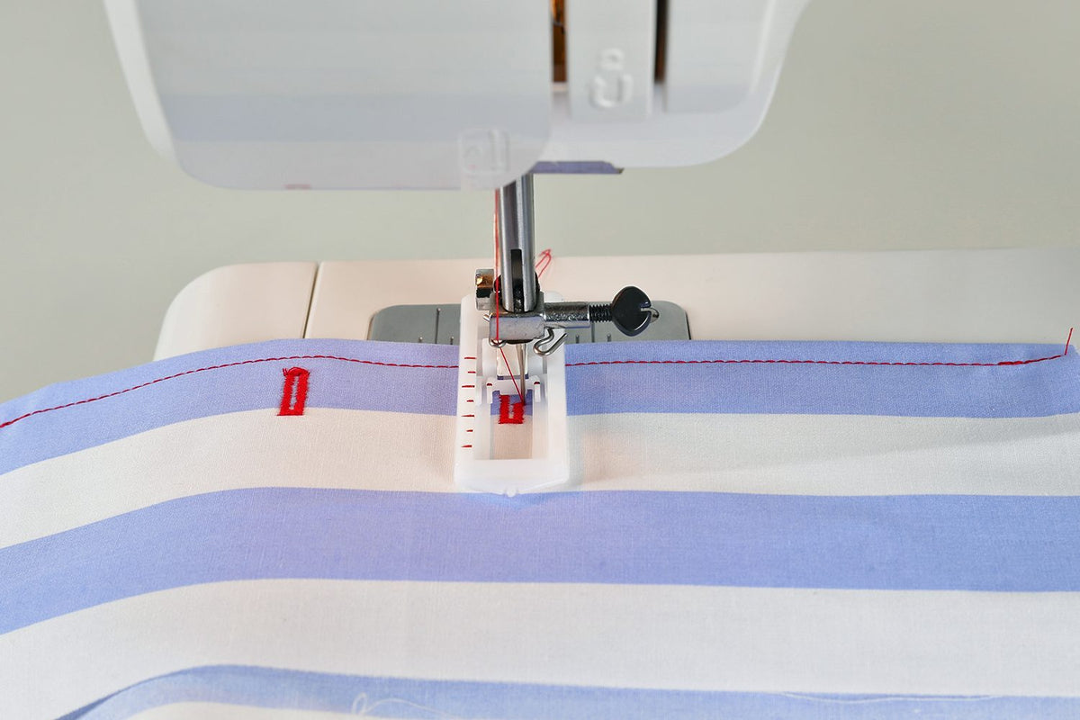 Close-up of a sewing machine needle and presser foot stitching a light blue and white striped fabric, with a red thread visible.