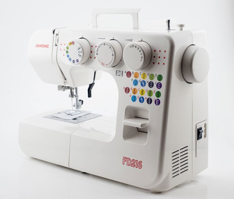 A white Janome FD216 sewing machine photographed on a clean white studio background. The machine has multiple white dials, a bed of buttons with multicolored lettering, a metal presser foot, and a side handle on top.