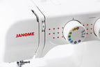 Close-up of a white Janome sewing machine showing the brand name in red and the stitch selector dial with colored indicator symbols.