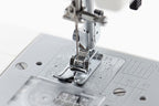 Close-up of a sewing machine needle and presser foot assembly on a light gray sewing machine bed with measurement markings.