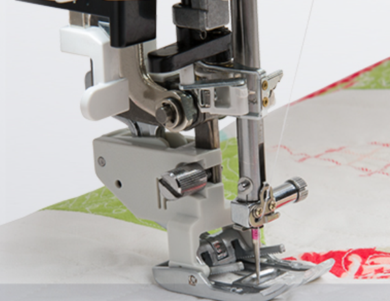 Close-up of a sewing machine presser foot and needle area stitching white fabric with a green and red pattern.