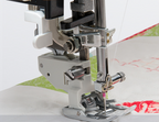 Close-up of a sewing machine presser foot and needle area stitching white fabric with a green and red pattern.