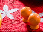 Two glossy orange ceramic salt and pepper shakers resting on a red quilted blanket with a white floral pattern.